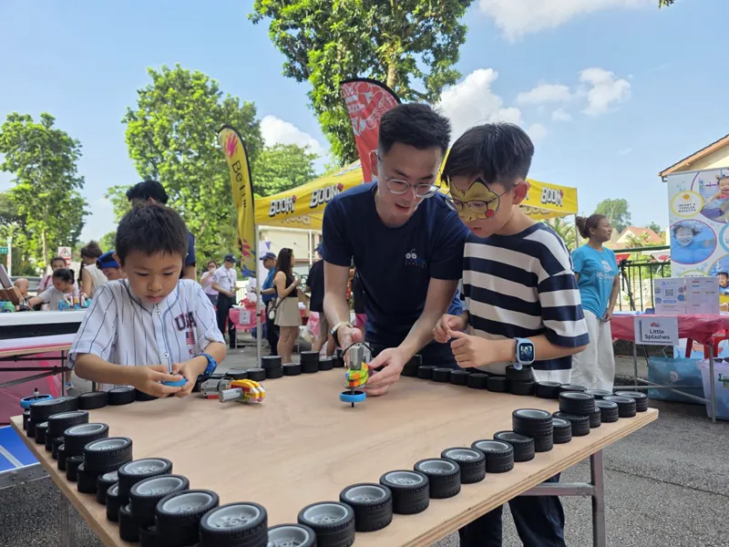 A Meta Robotics instructor helping a child test a spinning robot build at an outdoor community workshop